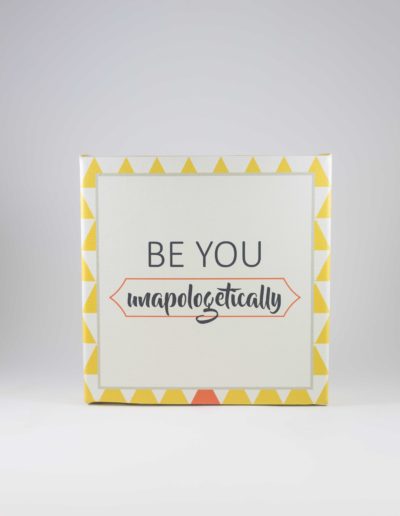 Square canvas with white background and yellow pyramid border, with one orange triangle at the bottom center. The words "BE YOU unapologetically" are in the center.