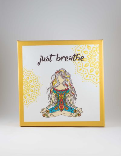 Square canvas with white background, yellow border, and a drawing of a women sitting in a meditative pose. The worlds "Just Breathe" are above her in a handwritten-style font. Mandala designs are in the background.